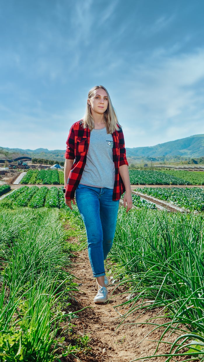 A blonde woman in casual attire walking through lush green farm fields on a sunny day.